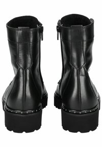 Botas de cuero negro hasta el tobillo con un tacón bajo, cierre de cremallera y acento de tachuelas a lo largo de la suela. Textura suave con un forro acolchado.