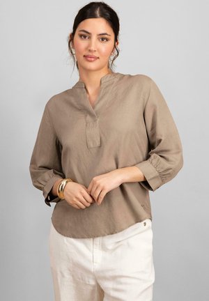 Blouse beige légère avec un col mandarin, des manches trois-quarts et un ourlet arrondi. Présente des coutures subtiles et de petits accents de boutons.