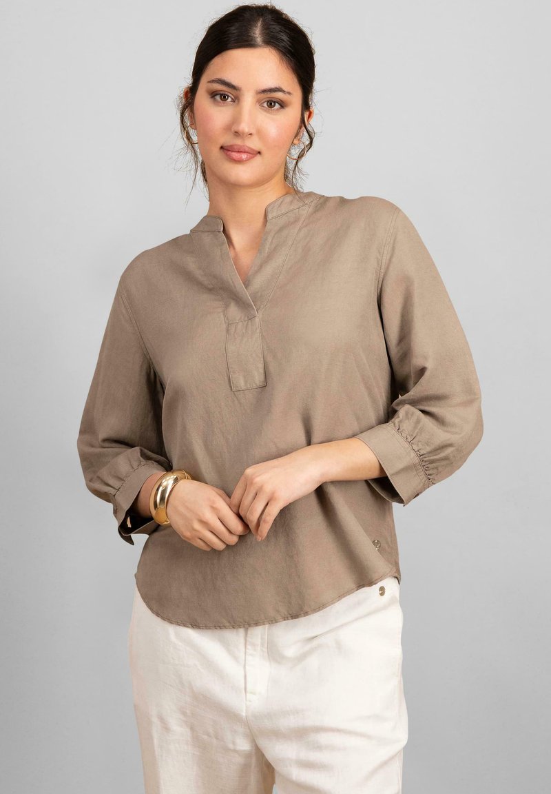 Beige, lehká blůza s mandarínkovým límcem, třičtvrtinovými rukávy a zaobleným lemem. Disponuje jemným prošíváním a malými knoflíkovými doplňky.