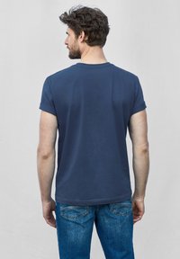 Tmavě modré tričko s krátkým rukávem z bavlny, s kulatým výstřihem a ohrnutými rukávy, nošeno s světle modrými džíny.