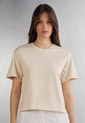 Beige short-sleeve t-shirt made of soft cotton with a crew neck. Straight cut and slightly loose fit, smooth texture with no visible patterns.