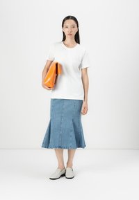 Witte T-shirt met korte mouwen, lichtblauwe denim flared rok en grijze instapschoenen. Houdt een grote oranje clutch vast. Eenvoudig en modern ontwerp.