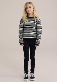 Svart och vit randig stickad tröja med långa ärmar; detaljer med vågkantad nederkant. Kombinerad med svarta smala jeans och svart-vita sneakers.