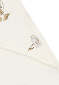 Un tissu en coton crémeux présente un motif de feuilles dans des couleurs atténuées. Une petite étiquette avec le logo de la marque "Jollein" est cousue sur le bord.