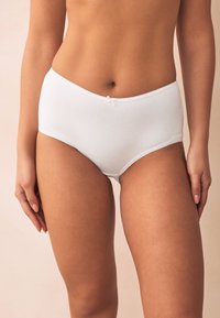 Culotte en coton blanc à taille haute avec une texture lisse, dotée d'une ceinture élastique à bords festonnés et d'un petit nœud décoratif à l'avant.