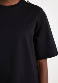 Black cotton t-shirt with a crew neckline, short sleeves, and plain texture. Features clean stitching along the seams.