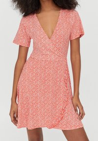 Robe portefeuille rouge à fleurs avec des manches courtes, un décolleté en V et une jupe évasée. Présente des motifs de fleurs blanches et un tissu texturé.