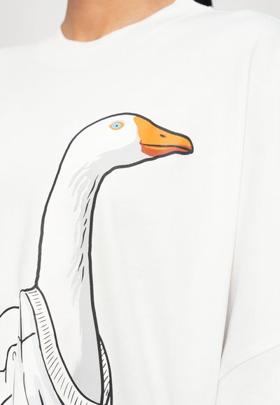 T-shirt blanc avec un graphique de la tête d'une oie, présentant un bec orange, un œil bleu et des contours noirs. Texture douce et lisse.