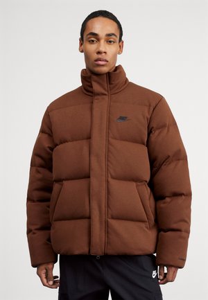 Bruine pufferjack met een hoge kraag, voorzien van een ritssluiting en een zwart Nike-logo op de linkerborst en zijzakken.