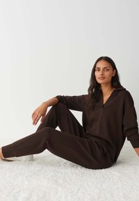 Brown loungewear set featuring a V-neck top with a relaxed fit and elastic waistband pants. Smooth texture with simple lines.