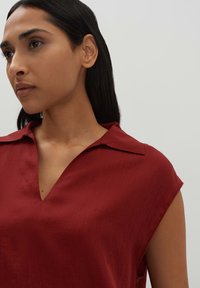 Maglietta rossa a maniche corte con scollatura a V e una sottile trama. Presenta un colletto classico e appare leggera e casual.