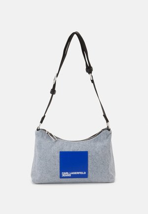 Sac d'épaule en denim à forme incurvée, écusson logo bleu, fermeture éclair argentée et sangle noire réglable. Tissu texturé avec des tons gris clair.