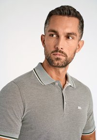 Harmaa polo-paita, jossa on teksturoitu kangas, kaksi nuppia, kontrastiväriset vihreät ja valkoiset raidat kauluksessa ja hihoissa.