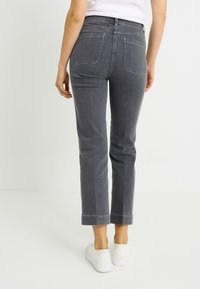 Vaqueros de mezclilla gris con ajuste estrecho, que cuentan con dos bolsillos traseros, detalles cosidos y un dobladillo recortado. Combinados con zapatillas blancas.