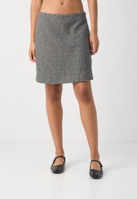 Mini-jupe grise avec un motif pied-de-poule, texture lisse et silhouette droite. Associée à des chaussures Mary Jane noires.