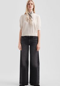 Crème gekamde gebreide top met korte mouwen, gecombineerd met hoog-waist zwarte wijde jeans. Sjaal geknoopt om de nek met florale print en hardware accenten.