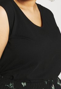 Top nero senza maniche con scollatura a V, realizzato in tessuto morbido, abbinato a una gonna floreale verde a motivi con vita elastica.