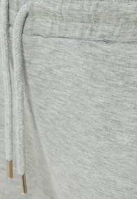Hellgraue Jogginghosen aus weichem Material, mit einem Kordelzug mit Metallenden und einer glatten Textur. Keine sichtbaren Logos oder Muster.
