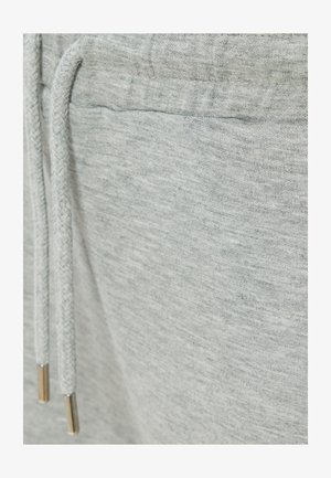 Jasnoszare dresy z miękkiego materiału, z sznurkiem ściągającym z metalowymi końcówkami i gładką teksturą. Brak widocznych logo lub wzorów.