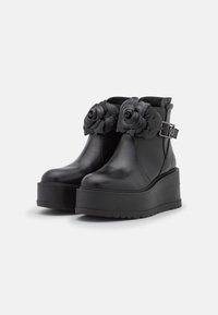 Botines de plataforma negros con suelas gruesas, correas de tobillo con hebillas y grandes adornos de rosa negra en la parte delantera.