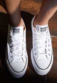 Sneaker di tela bianca con dettagli neri, dotate di punta di gomma, occhielli in metallo e lacci, con il logo Converse All Star.