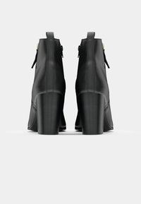 Stivaletti neri in pelle con una finitura liscia, tacco a blocco alto e dettagli con zip, caratterizzati da un design minimalista e nessun motivo visibile.