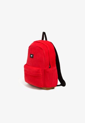 Mochila de pana roja con forma redondeada, correas negras, un gran bolsillo frontal y una etiqueta de logo en la parte delantera. La parte inferior es marrón.