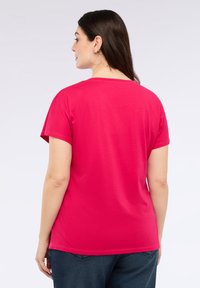 Fuksia puuvillapaita lyhyillä hihoilla ja pyöreällä kaula-aukolla, esitelty takaa, rento istuvuus ja vähäiset ommelvahvistukset.