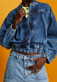 Beschnitten jeansjacka i medelblått med puffade ärmar, med knäppning och elastisk midja, bärs med högmidjade jeans.