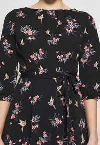 Svart klänning med blommönster i rosa blommor och fåglar. Plisserad halsringning, trekvartsärmar och knuten midja. Lättviktsmaterial.