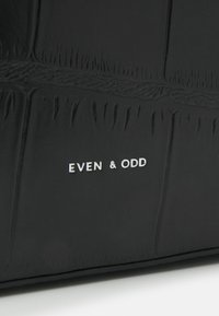 Sac à main noir en simili cuir texturé, présentant un motif crocodile. Logo "EVEN & ODD" en relief sur le devant. Fini lisse.