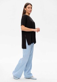 Czarny top z krótkim rękawem z rozcięciami po bokach, w połączeniu z jasnoniebieskimi spodniami dzwonami. Miękka, gładka tkanina o luźnym kroju.