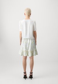 Hvit teksturert cropped skjorte kombinert med et lys blomstermønstrete skjørt med volangkant og svarte stroppesandaler.