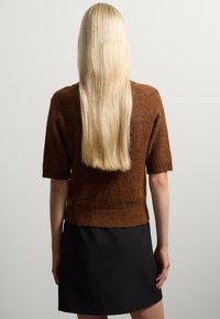 Maglione corto a maniche corte di colore marrone con orlo a costine, abbinato a una gonna nera. Capelli lunghi e lisci di colore biondo scendono lungo la schiena.