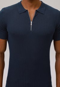 Marinblå, ribbad polo med korta ärmar, med en framzip och en texturerad yta. Mjuk, elastisk tyg.