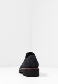 Dunkelblaue Wildlederschuhe mit strukturiertem Finish, verziert mit Broguedetails und einer dicken schwarzen Sohle für Stabilität. Rückansicht dargestellt.