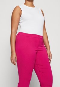 Vit ärmlös topp och rosa figursydda byxor med knäppning. Byxorna har en slät textur och skräddarsydd passform.