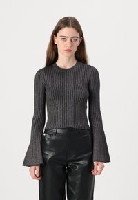 Zwarte geribbelde longsleeve top met uitlopende mouwen, gemaakt van een metallic textuurstof. Draagt bij hoge taille zwarte leren broek.