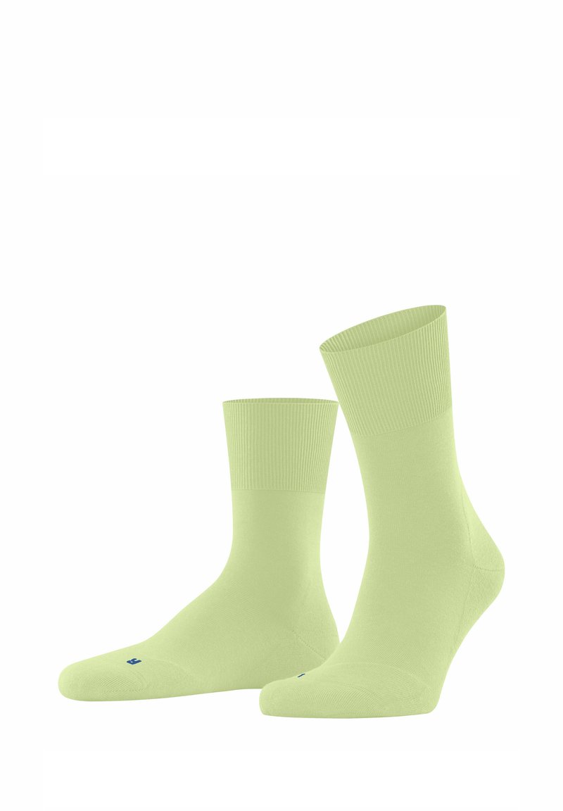 Chaussettes en coton vert clair avec une texture lisse, des côtes aux poignets et des orteils renforcés, arborant un petit logo bleu sur la semelle.