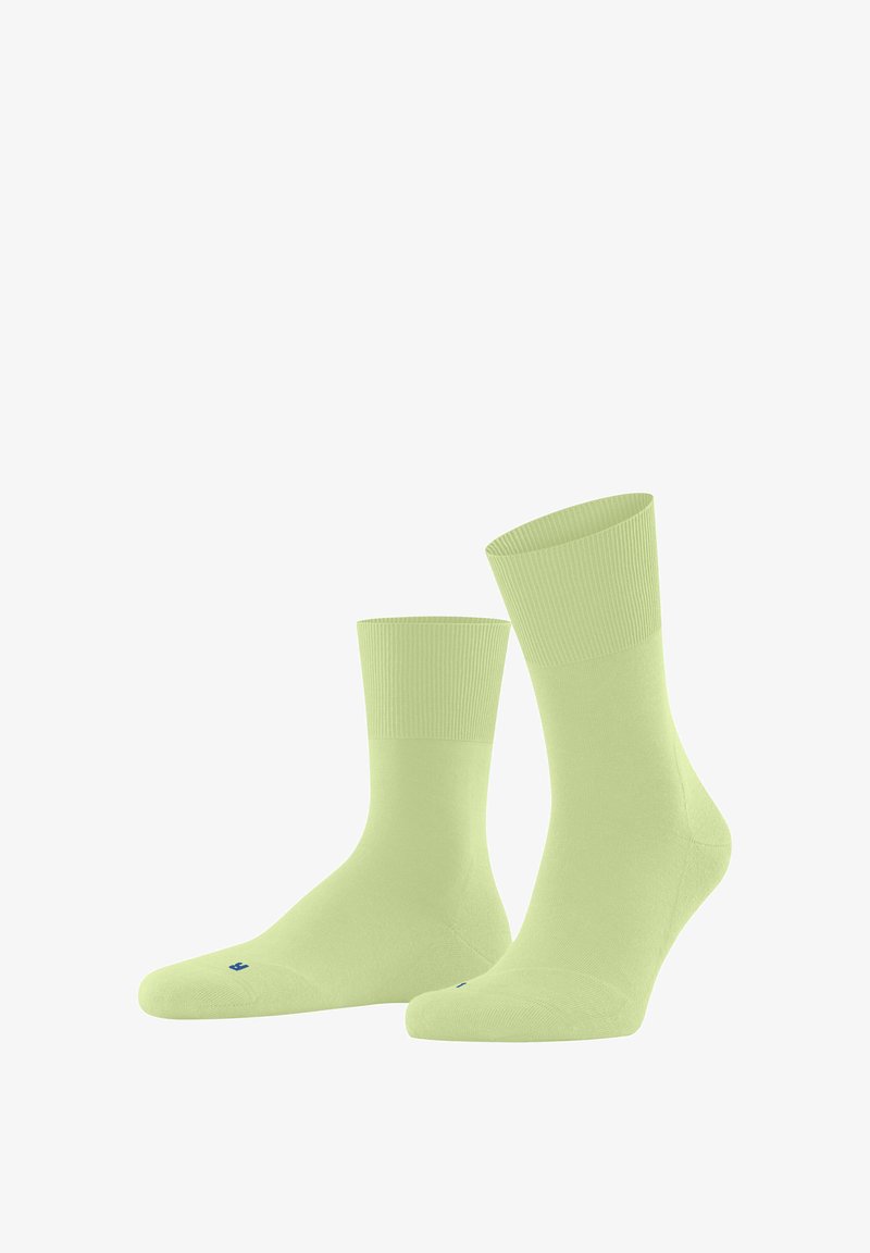 Lichtgroene katoenen sokken met een gladde textuur, geribbelde boorden en verstevigde tenen, met een klein blauw logo op de zool.