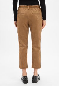 Braune Wildlederhosen mit leicht zulaufendem Bein, elastischem Bund und zwei Gesäßtaschen. Kombiniert mit schwarzen Plateauschuhen.