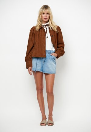 Bruine suède jas met pofmouwen, knoopsluiting; wit topje, lichtblauwe denim shorts en lichtbruine instapschoenen.