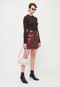 Brun langermet topp med volanghals, rød kunstskinn mini-skjørt med sølvknapper, svarte ankelstøvletter og kremfarget crossbody veske.