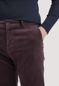 Paarse corduroy broek met een ribbelstructuur, voorzakken en een enkele knoopsluiting, gecombineerd met een donker marineblauw shirt met lange mouwen.