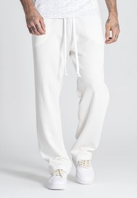 Pantalones de chándal blancos con textura de waffle, cintura elástica y cordón; corte relajado; combinados con zapatillas blancas.