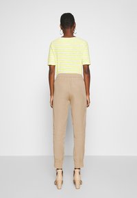 Geel en wit gestreepte top met korte mouwen, gedragen met beige elastische taillebroek. De outfit wordt aangevuld met naakte hoge hakken sandalen.