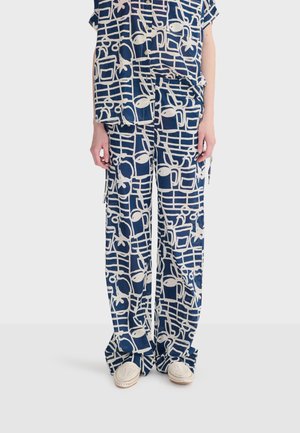 Løse bukser med blåt og hvidt abstrakt mønster kombineret med matchende kortærmet skjorte med knapper og hvide vævede slip-on sko.