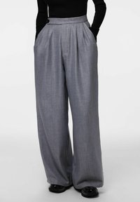 Szare spodnie o szerokich nogawkach wykonane z fakturowanej tkaniny, z plisami, kieszeniami po bokach oraz pojedynczym zapięciem na guzik w pasie.