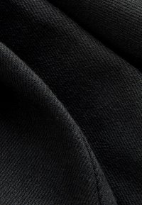 Černá látka s hladkou texturou, obsahující tkaný vzor a zavěšené záhyby, vykazující různé odstíny tmavosti a odraz světla.