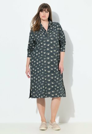 Robe longue et sombre avec un col zippé, ornée de motifs circulaires clairs. Présente des manches longues et des fentes sur les côtés pour faciliter les mouvements.
